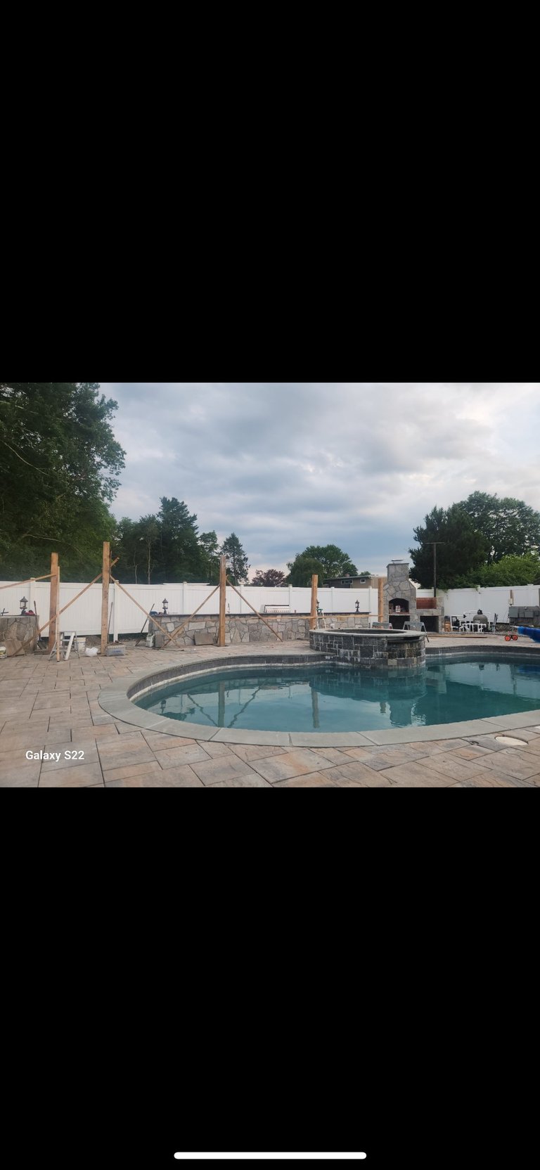 Outdoor residential swimming pool under renovation with wooden support beams, surrounded by patio and construction equipment